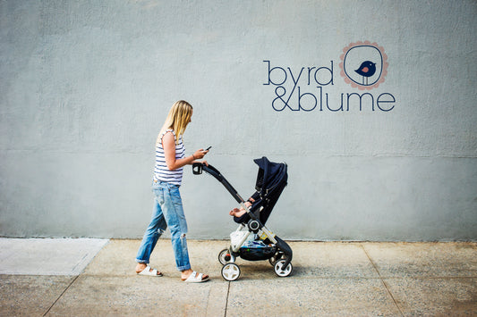 mother walking baby while answering work emails. Beautiful Byrd and Blume brand on the wall behind